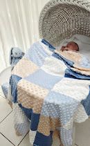 Baby sleeping in a wicker Moses basket with a blue and beige patchwork quilt blanket.