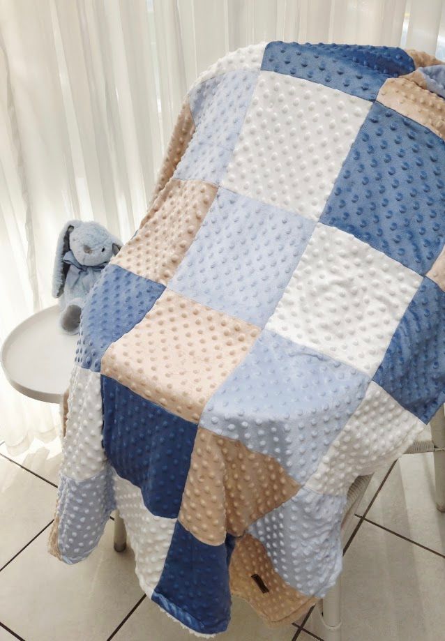 Soft minky patchwork baby blanket in blue, white, and beige with a small blue bunny stuffed animal on a white chair.