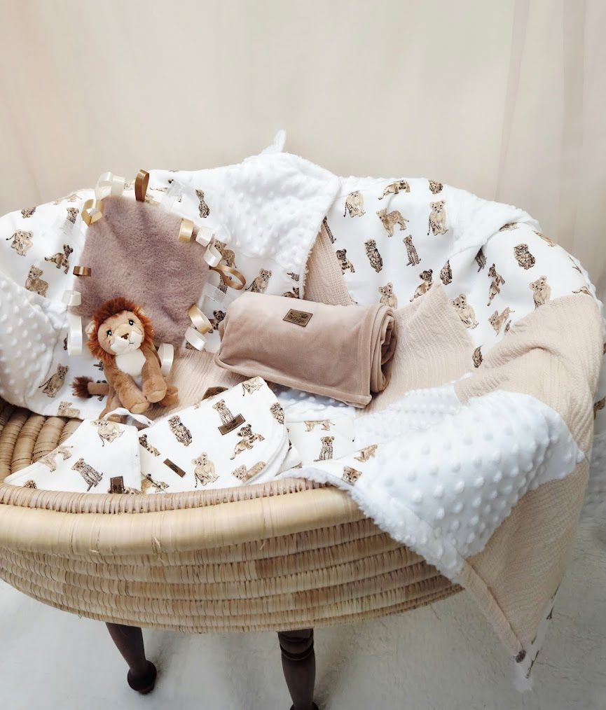 Neutral beige baby nursery set with animal print blankets, minky dot fabric, and a plush lion toy in a wicker Moses basket.