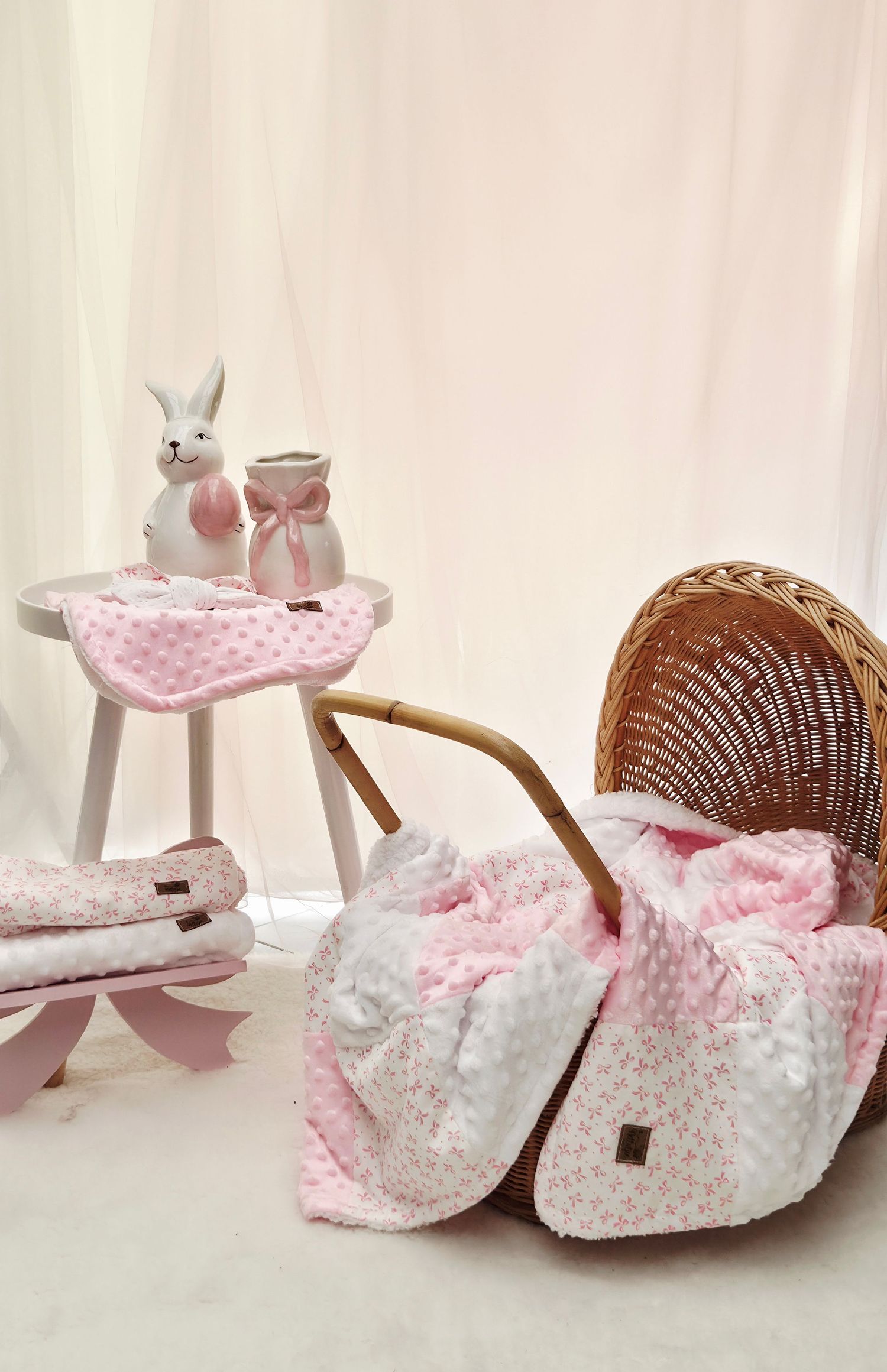 Pink floral baby blanket in wicker Moses basket with bunny figurines on white stool, soft nursery decor set.