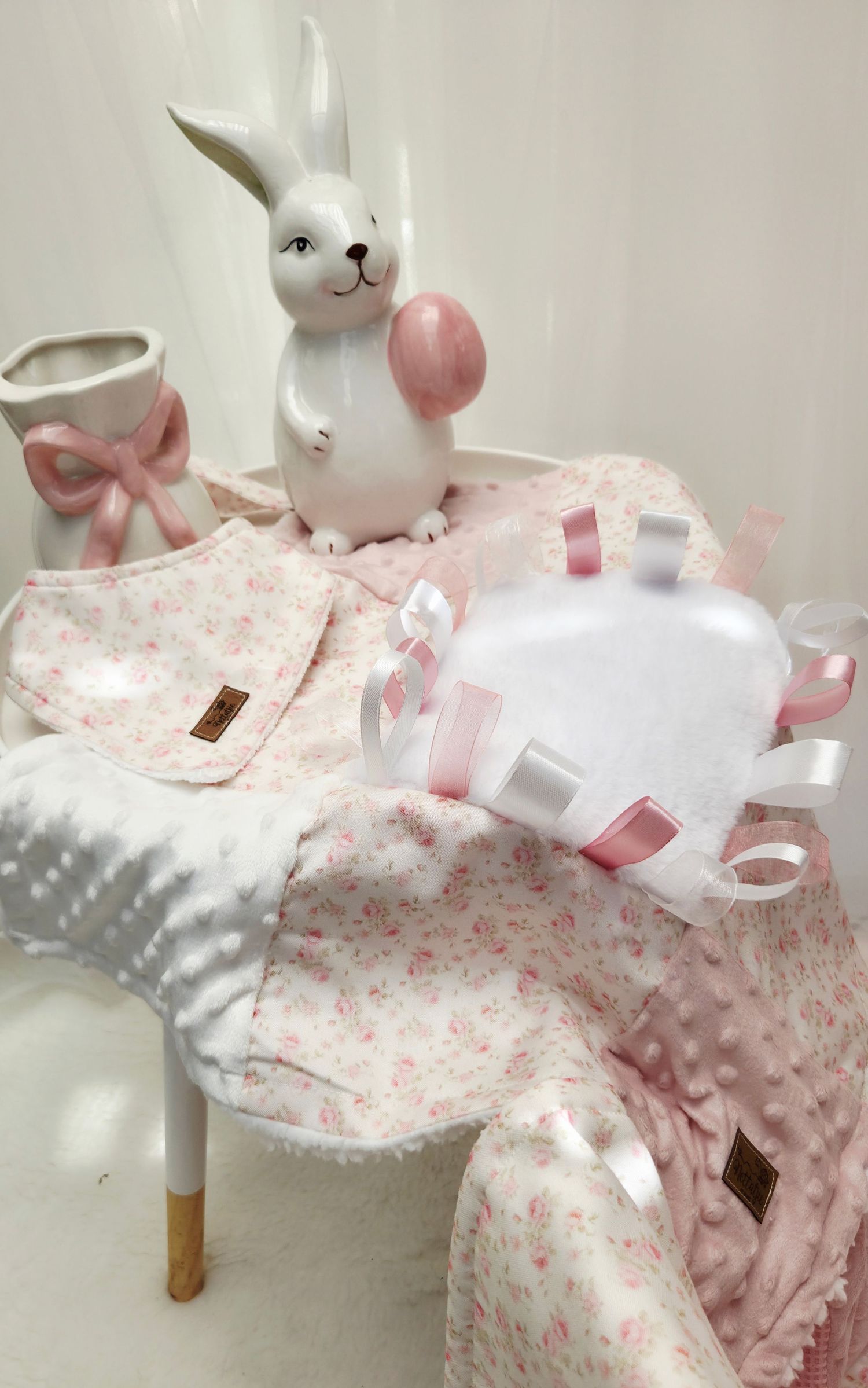 Pink floral baby gift set with bunny figurine, bib, blanket, and ribbon toy for newborns.
