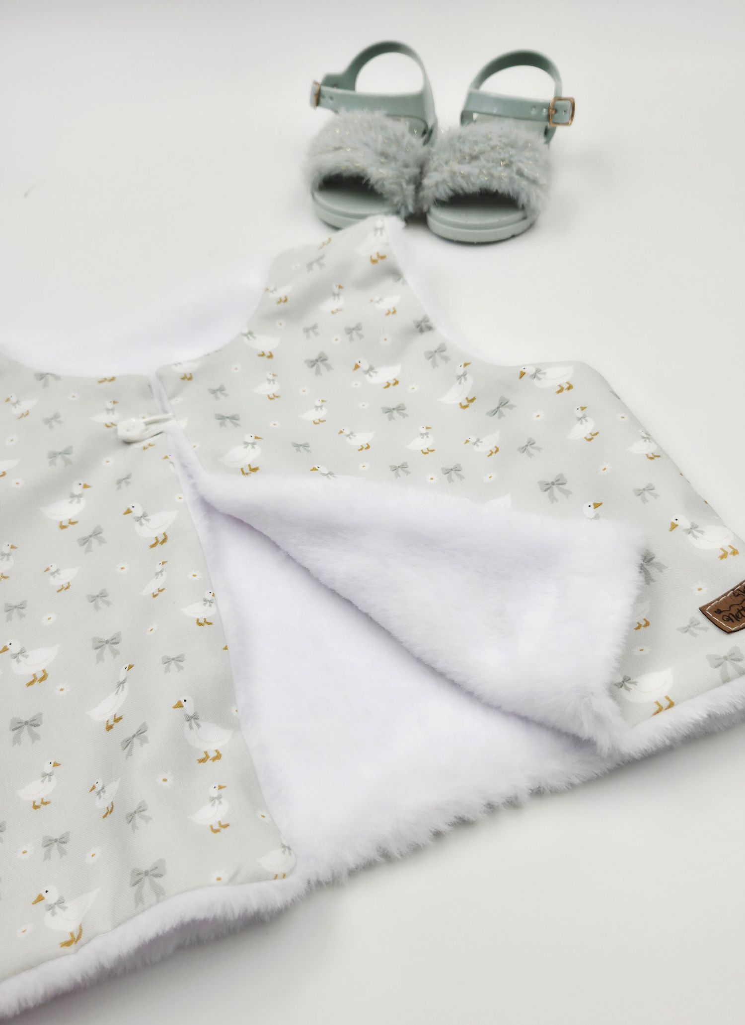 Soft gray baby bib with white sherpa lining featuring a delicate lamb print, displayed with matching mint green sandals.