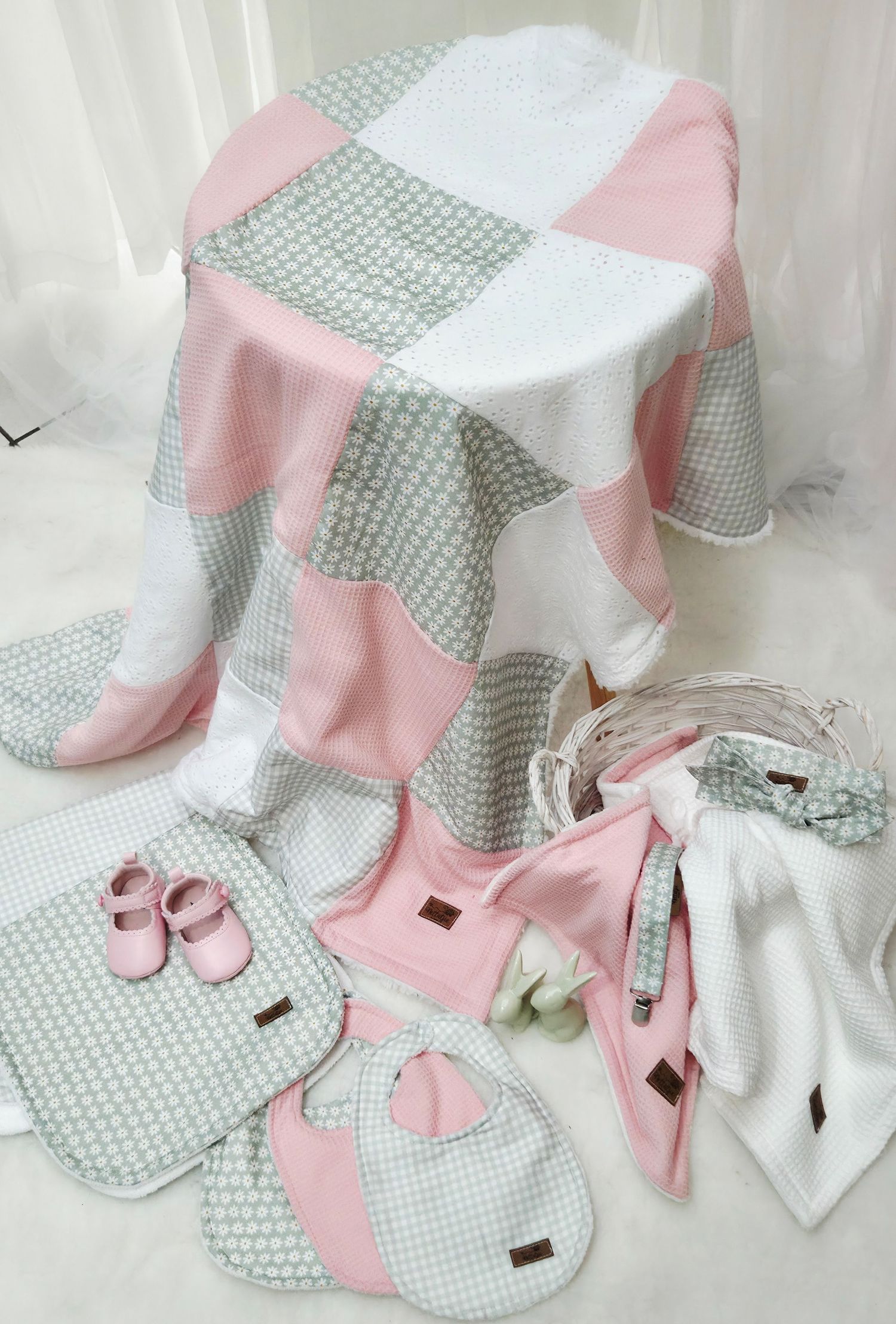 Pink and gray patchwork baby gift set with blanket, bib, booties, and accessories on white background.