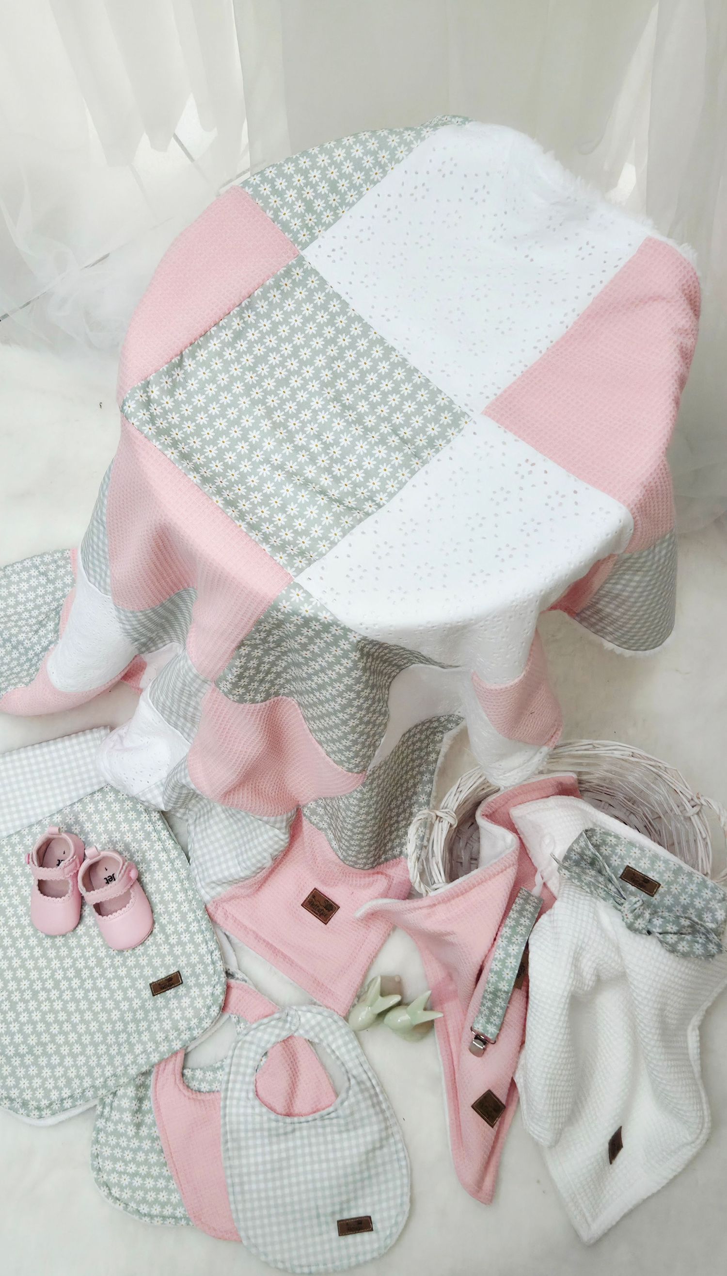Pink and gray patchwork baby quilt set with bibs, booties, and accessories arranged on white background.
