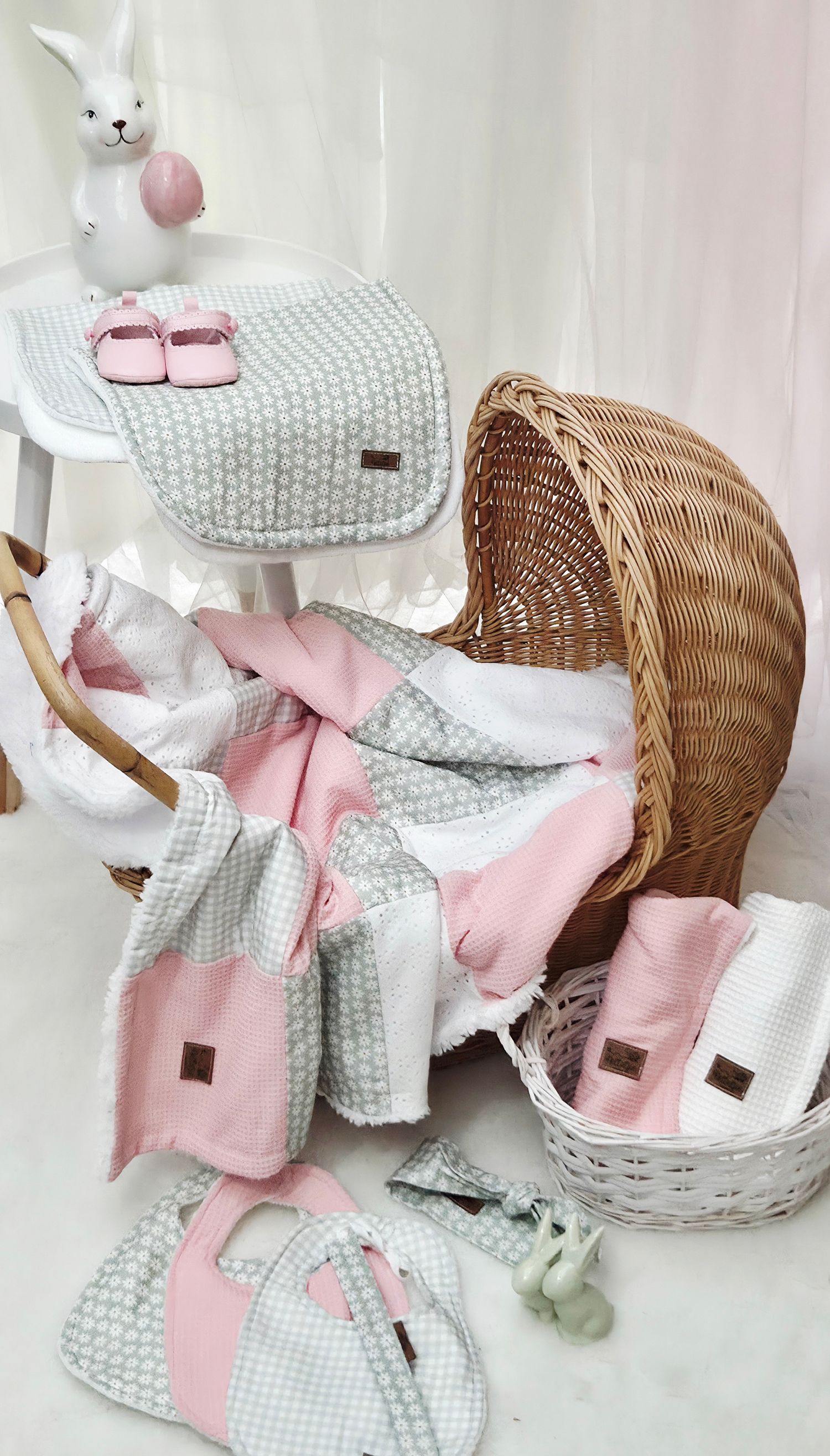 Pink and gray baby gift set with blanket, shoes, and accessories in a wicker bassinet with bunny decor.