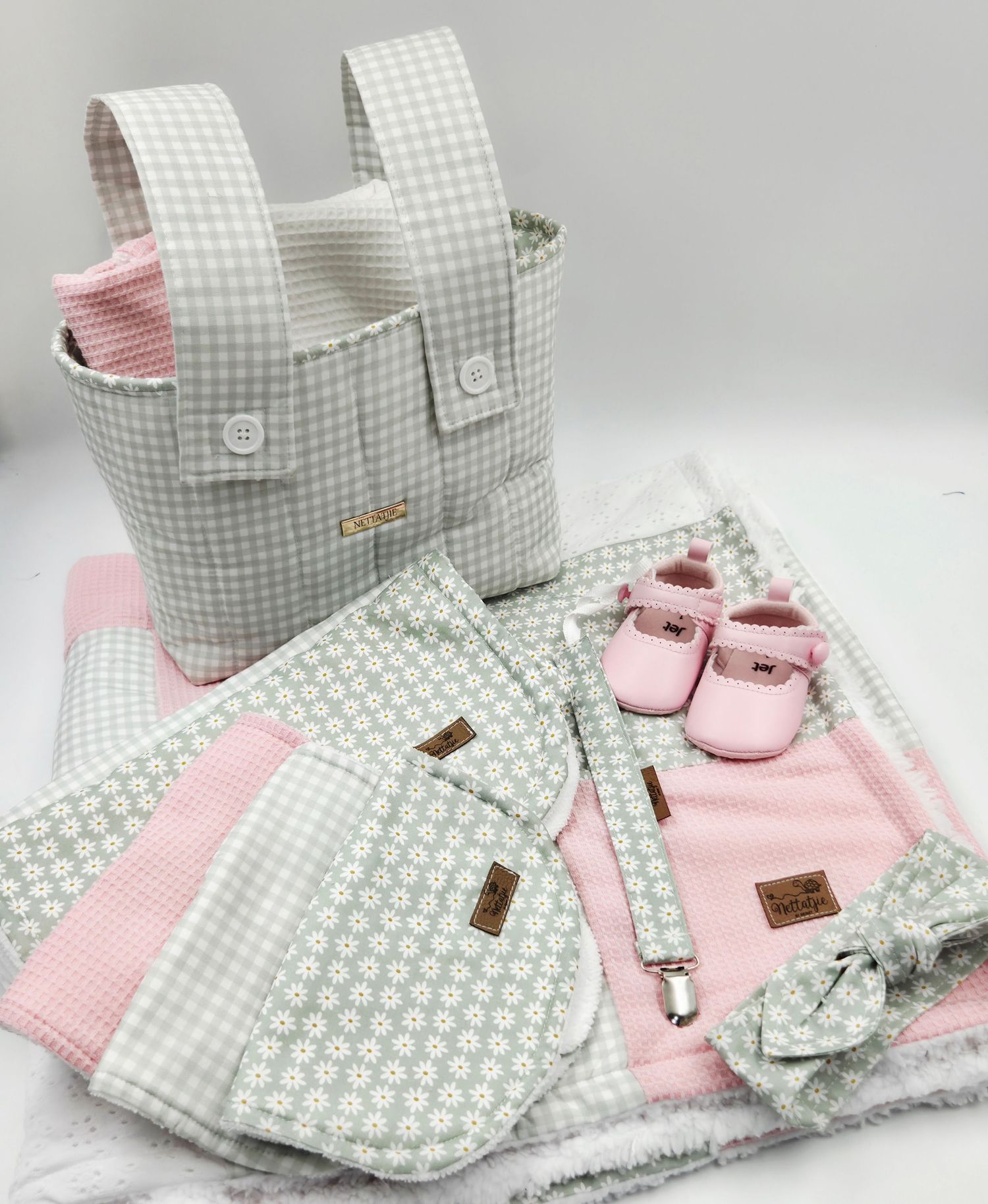 Pink and gray baby gift set with diaper bag, booties, blanket, bib, and accessories in gingham pattern.