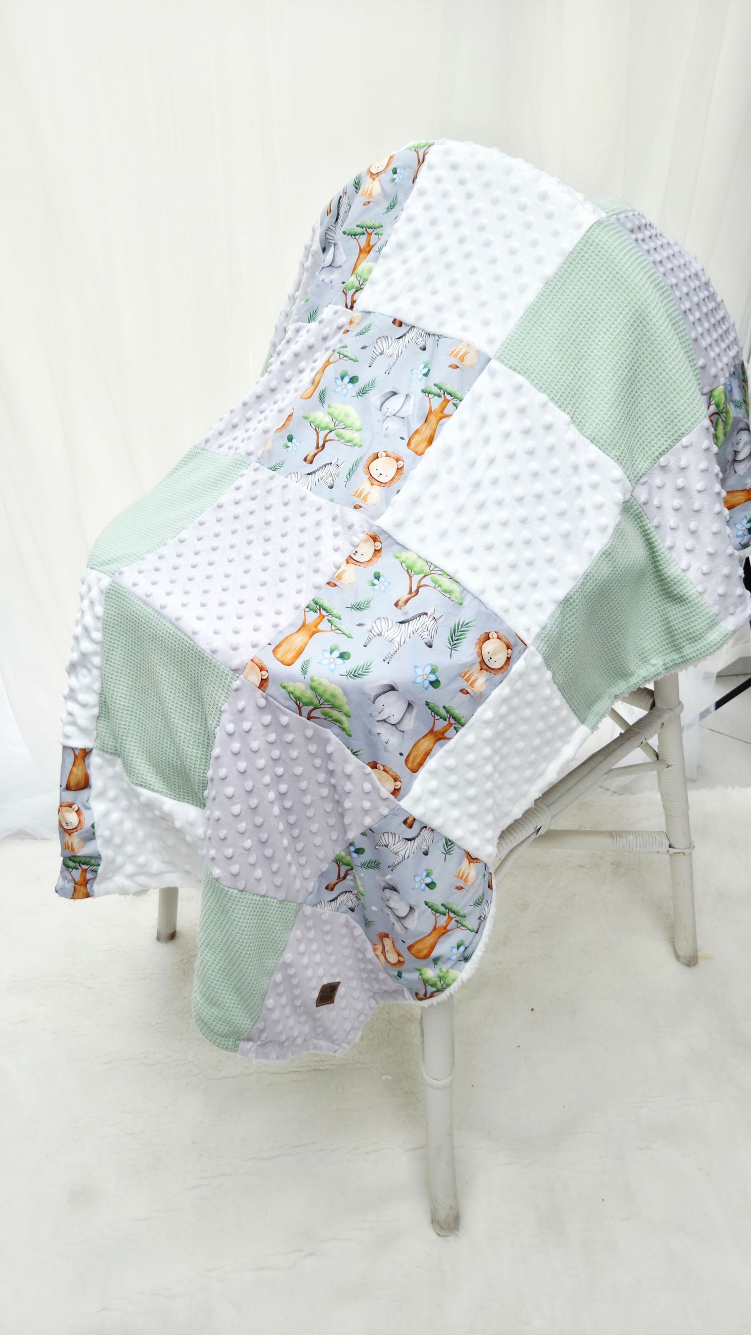 Handmade patchwork baby quilt with safari animals, mint green, white, and gray minky fabric squares on a chair.