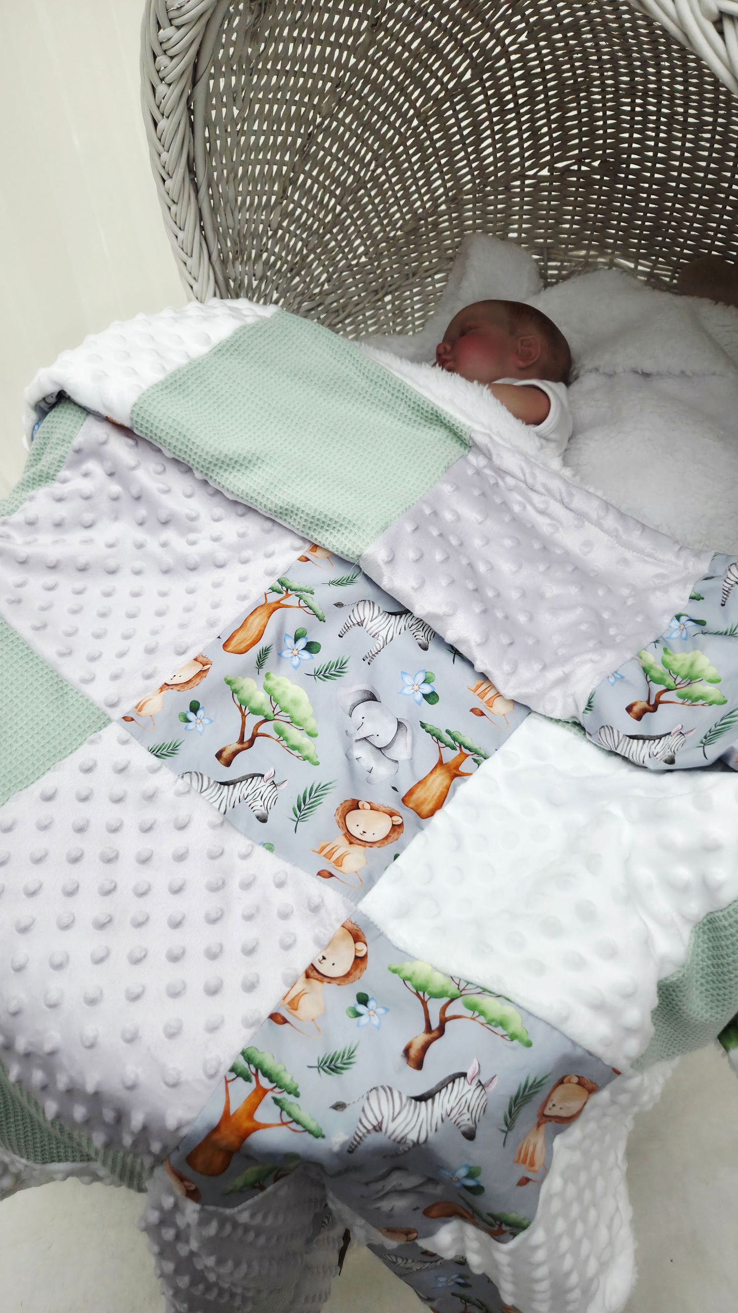 Newborn baby wrapped in a patchwork quilt with safari animals, mint green, white minky dots in a wicker Moses basket.