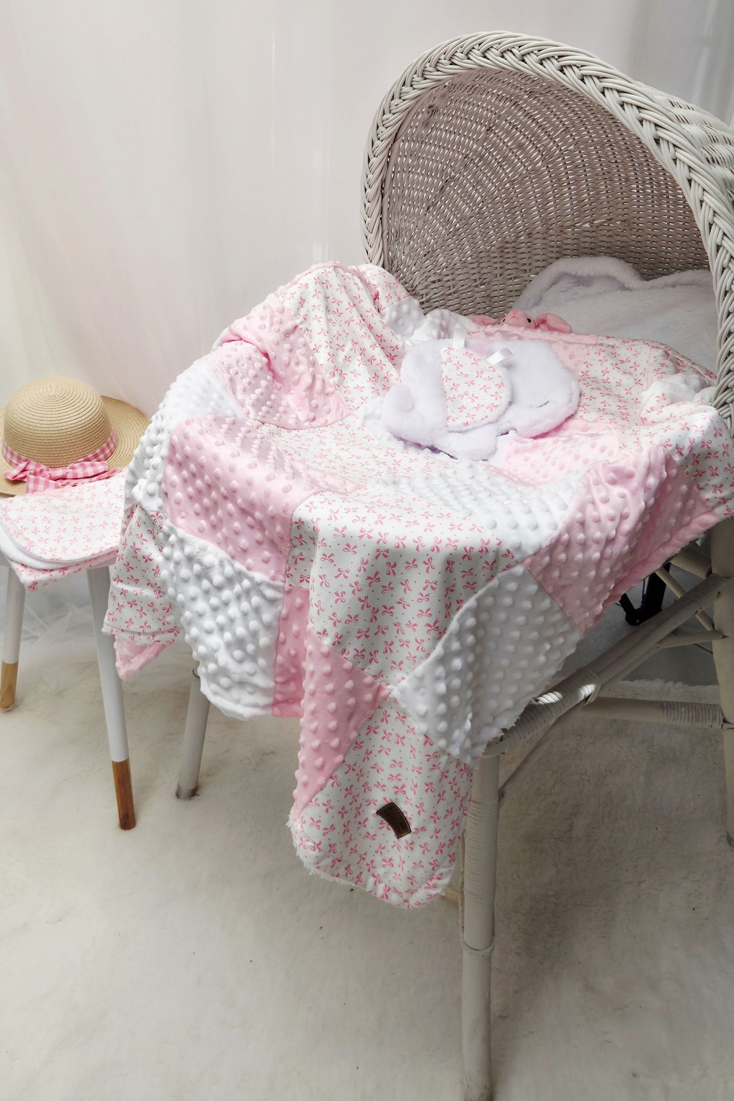 Pink floral baby blanket with minky dot fabric draped over a wicker chair, with matching hat and booties.