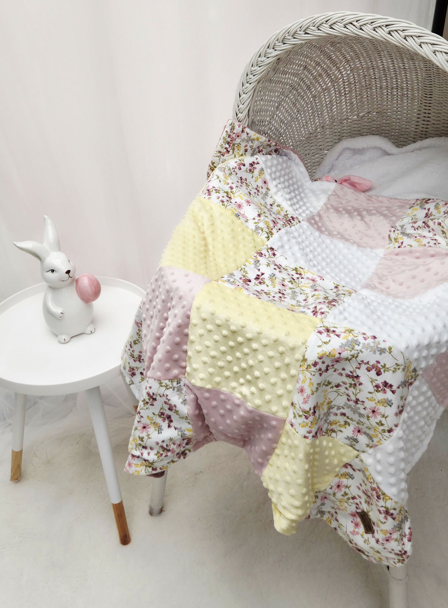 Pastel patchwork baby quilt with floral and minky fabric draped over a wicker chair beside a white bunny figurine.