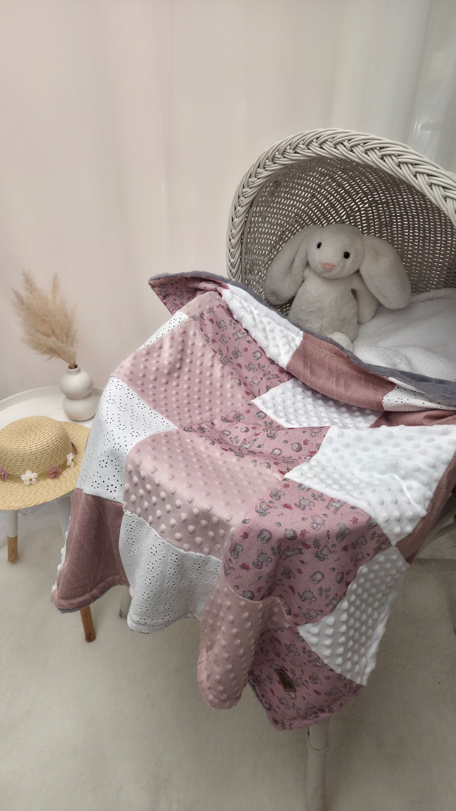 Pink patchwork baby quilt with minky fabric draped over wicker chair with stuffed bunny toy.
