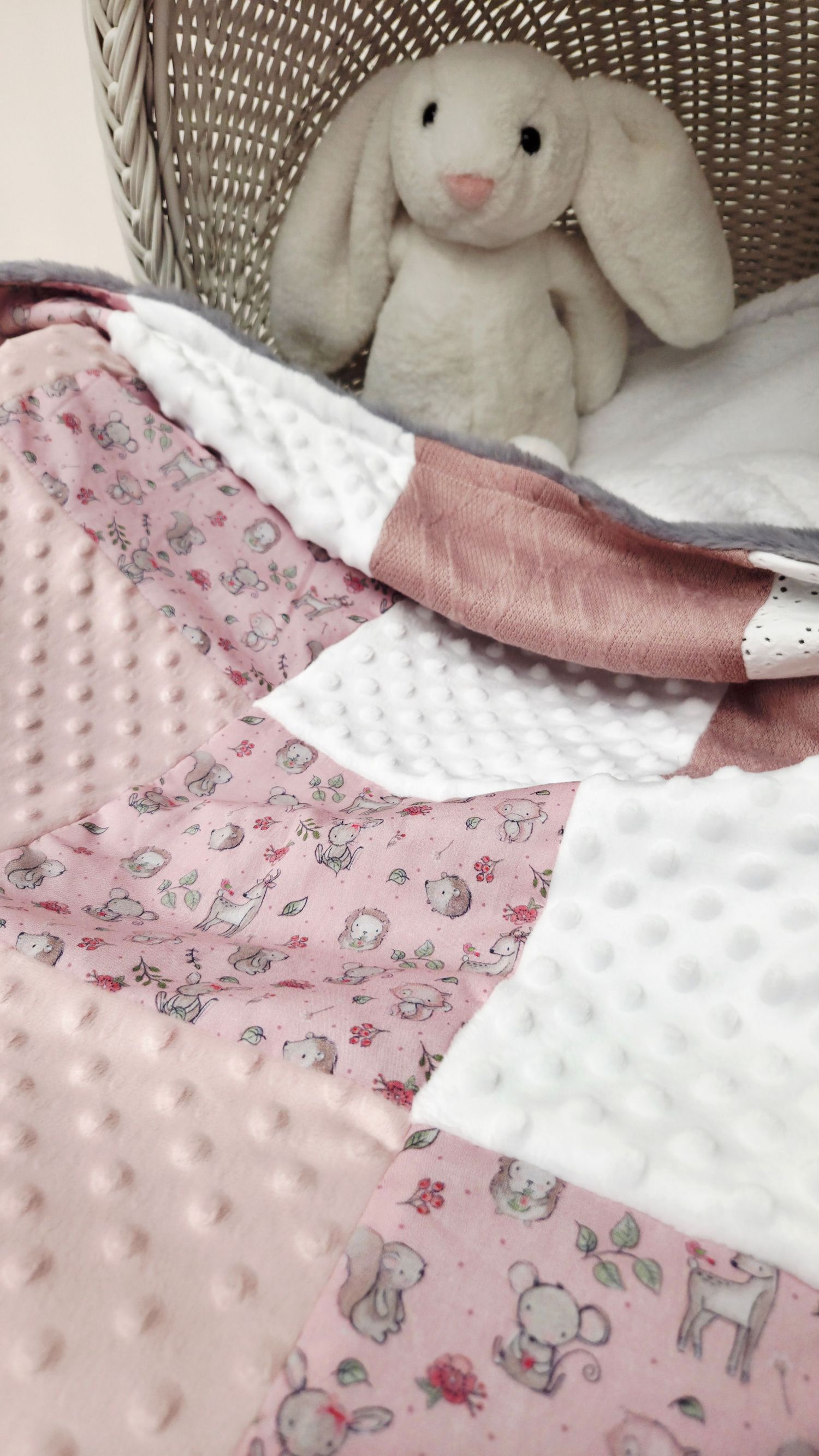 Pink patchwork baby blanket with animal print and minky dots, displayed with a white plush bunny in a wicker basket.