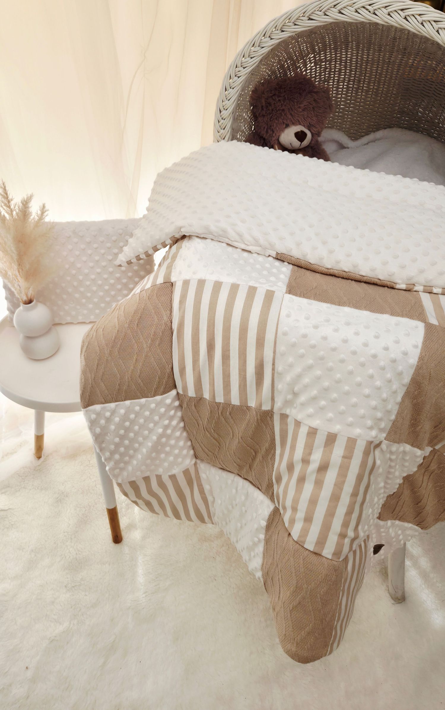 Neutral beige and white patchwork baby quilt draped over a wicker bassinet with a teddy bear.