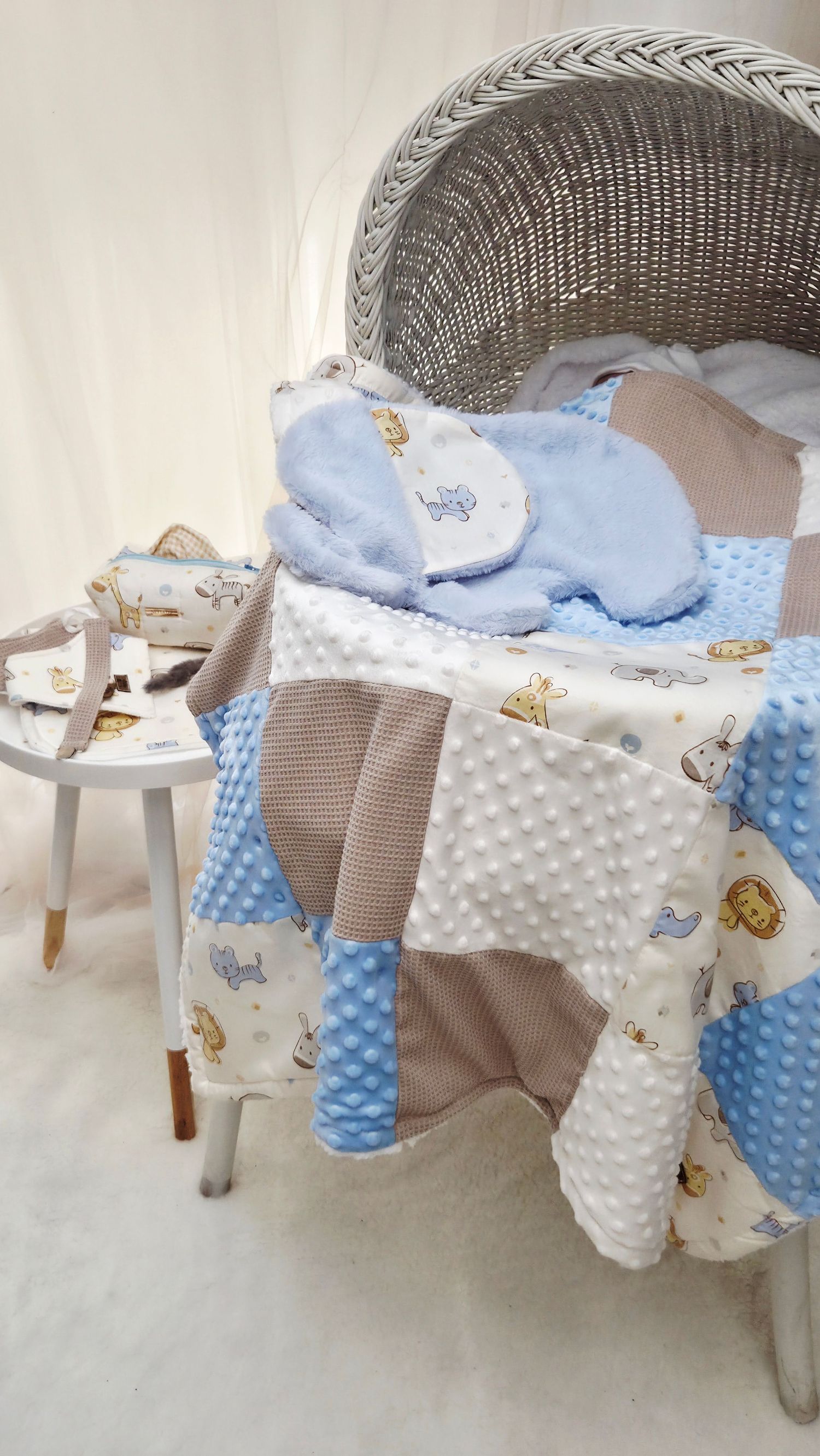 Baby patchwork quilt in blue, beige, and white with animal print beside a wicker bassinet.
