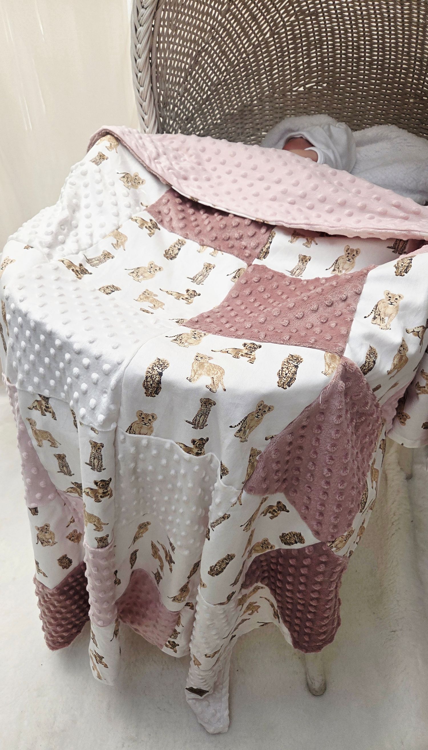 Pink and white patchwork baby quilt with animal print and minky dot fabric draped over a wicker bassinet.
