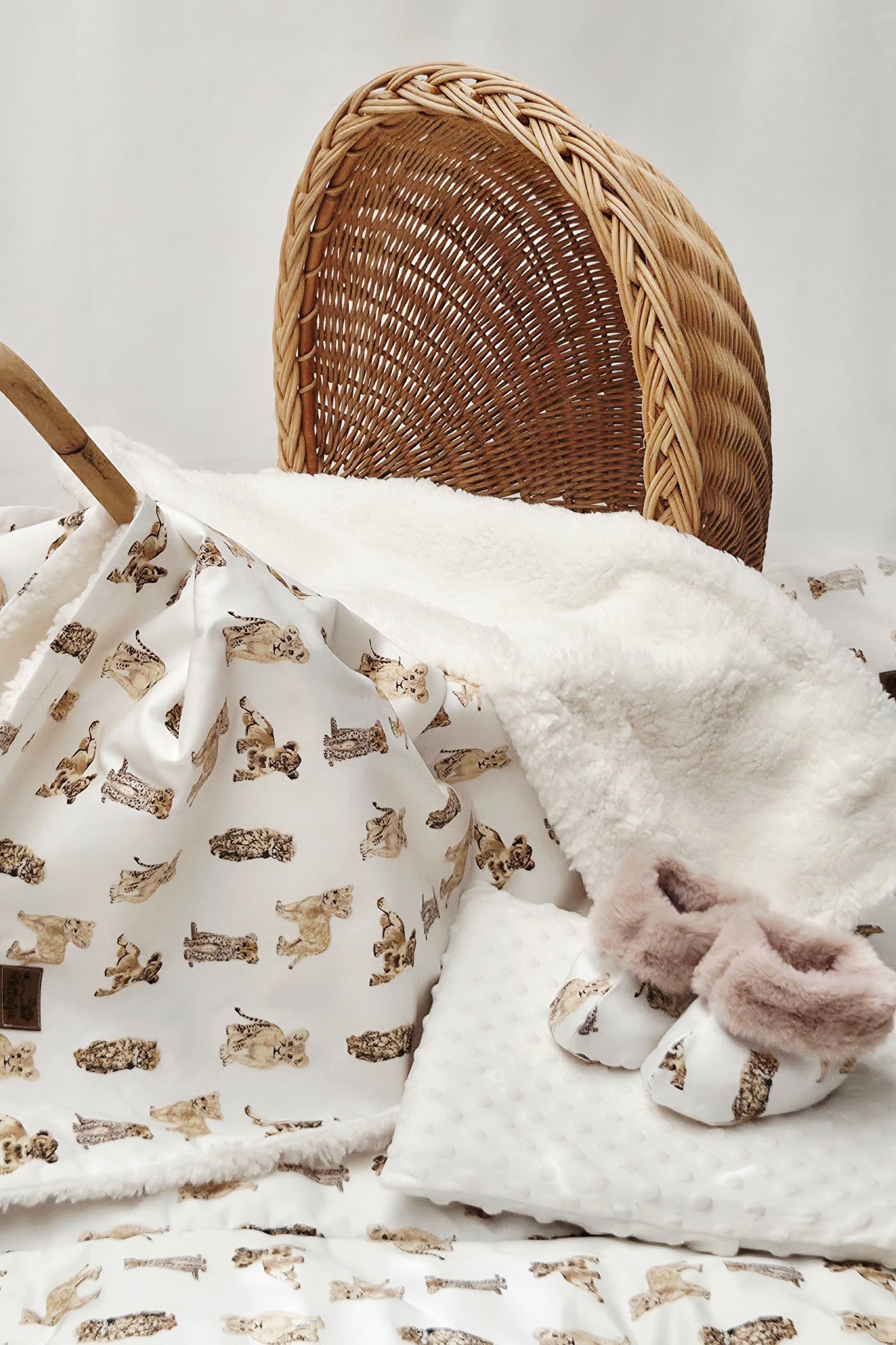 Baby blanket and booties with animal print beside a wicker bassinet, perfect for a neutral nursery.