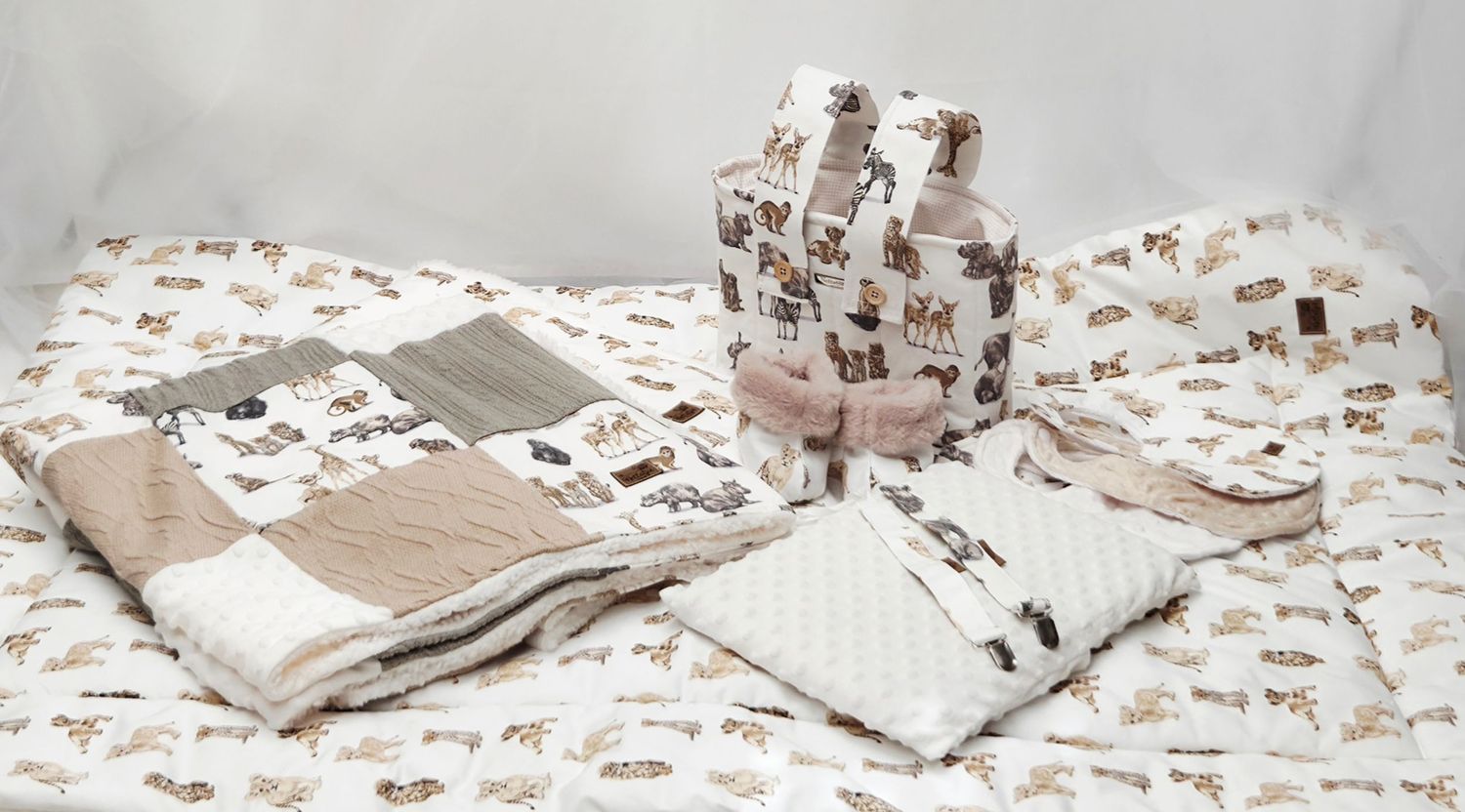 Baby bedding set with woodland animal print featuring blanket, pillow, and accessories in neutral beige and brown tones.