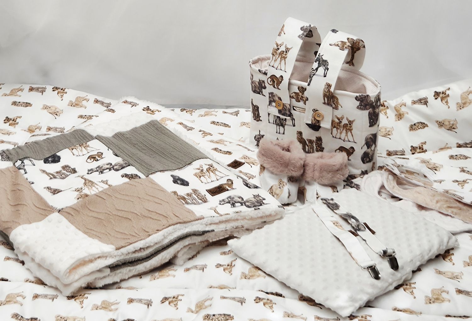 Neutral-toned baby gift set featuring a patchwork quilt, minky blanket, diaper bag, and pink booties with woodland animal prints.