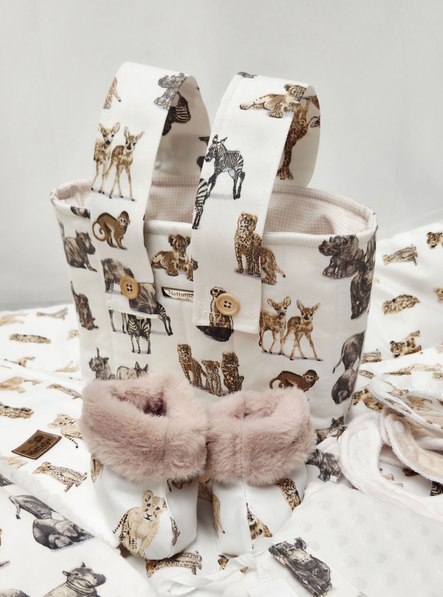 White fabric storage basket with animal print, decorated with buttons, displayed with matching fabric and pink faux fur slippers.