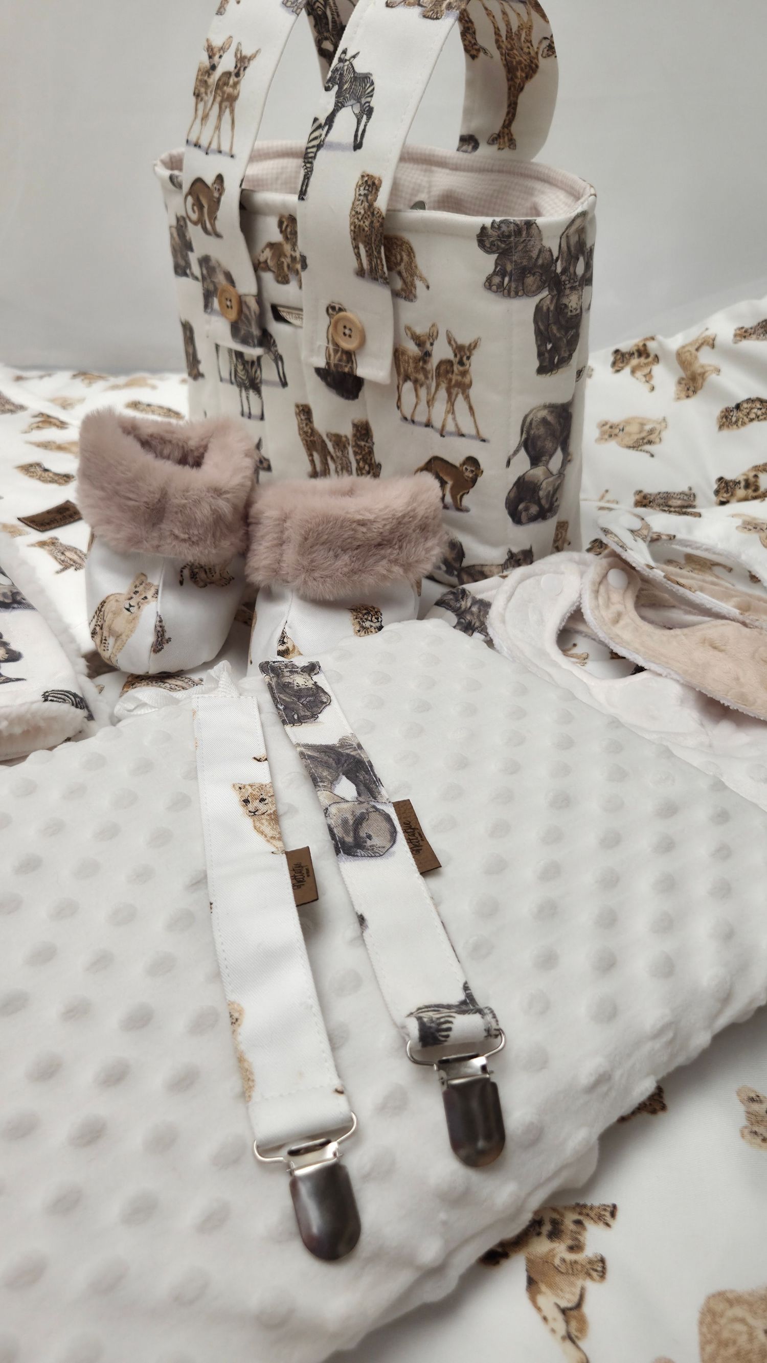Baby gift set with safari animal print blanket, booties, suspenders, and bag in neutral beige tones.