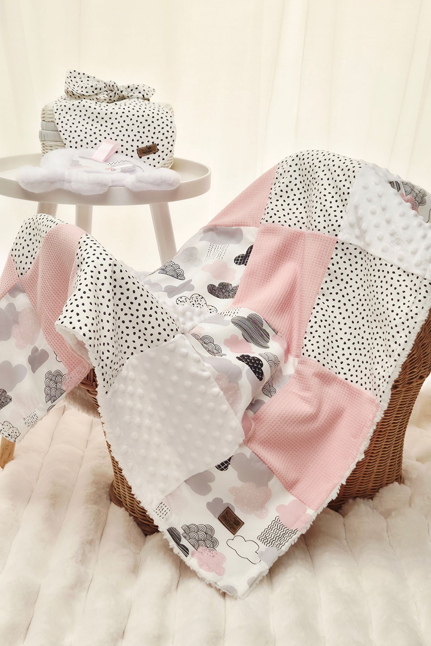 Pink and white patchwork baby quilt with polka dots and elephant print draped over a wicker basket.