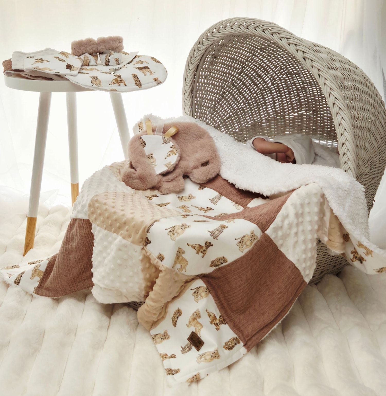 Cozy baby bassinet with neutral teddy bear blanket set, plush giraffe toy, and matching accessories in warm beige tones.
