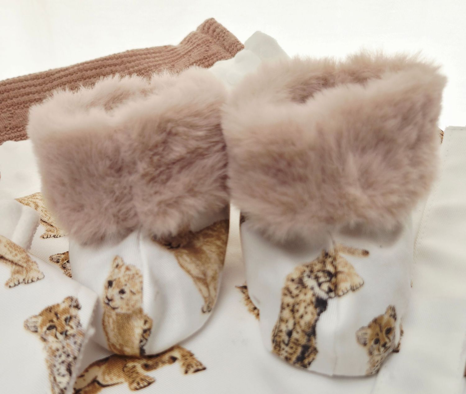 Adorable baby booties with fluffy fur trim and cheetah print fabric, displayed on a matching cheetah print blanket.