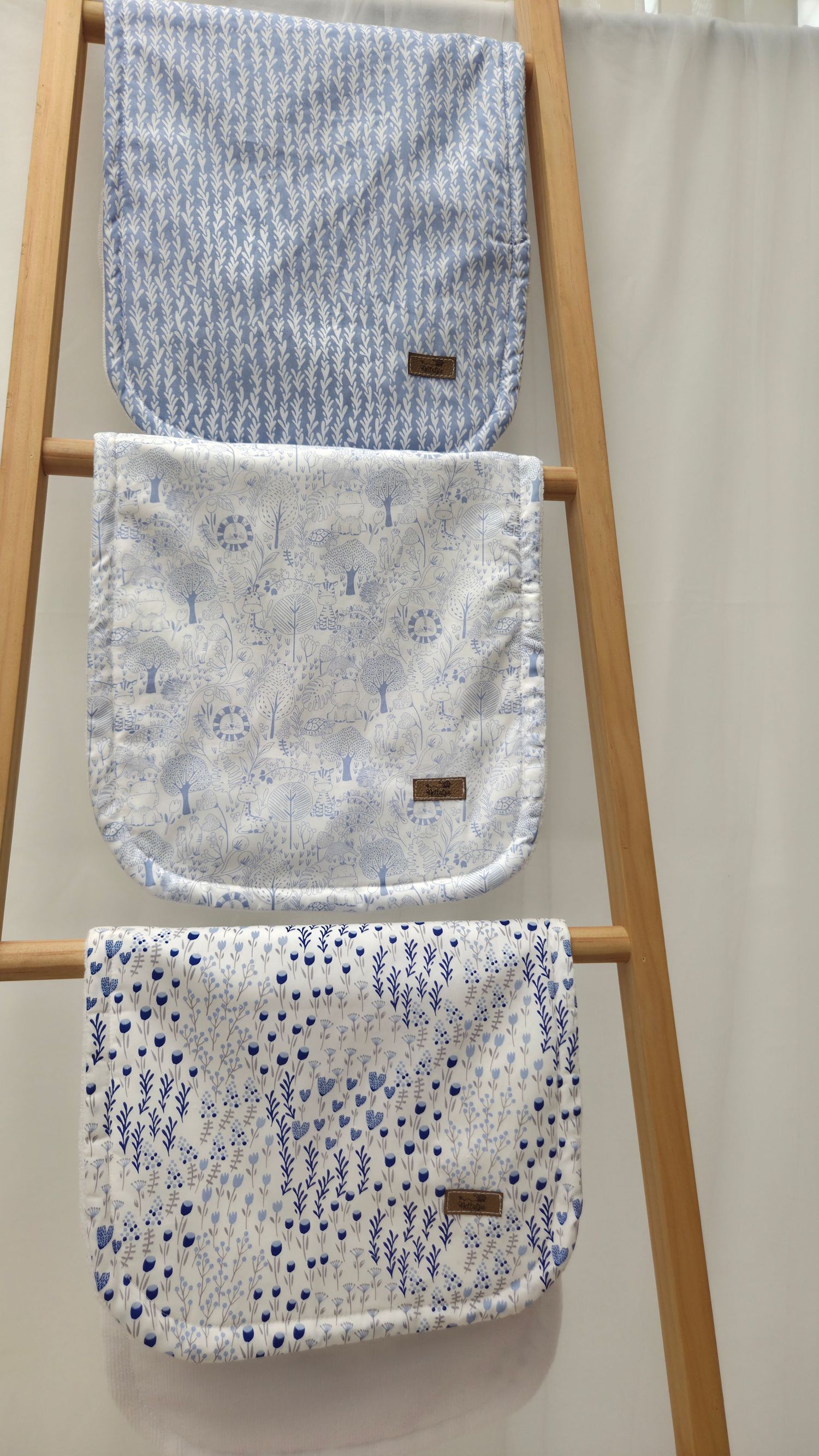 Three blue and white patterned baby burp cloths hanging on a wooden ladder display.