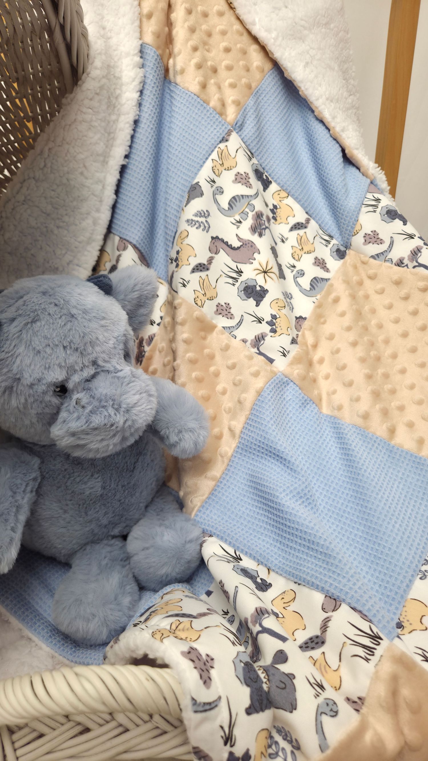 Blue and beige patchwork baby quilt with dinosaur print fabric, displayed with a soft blue elephant stuffed animal.