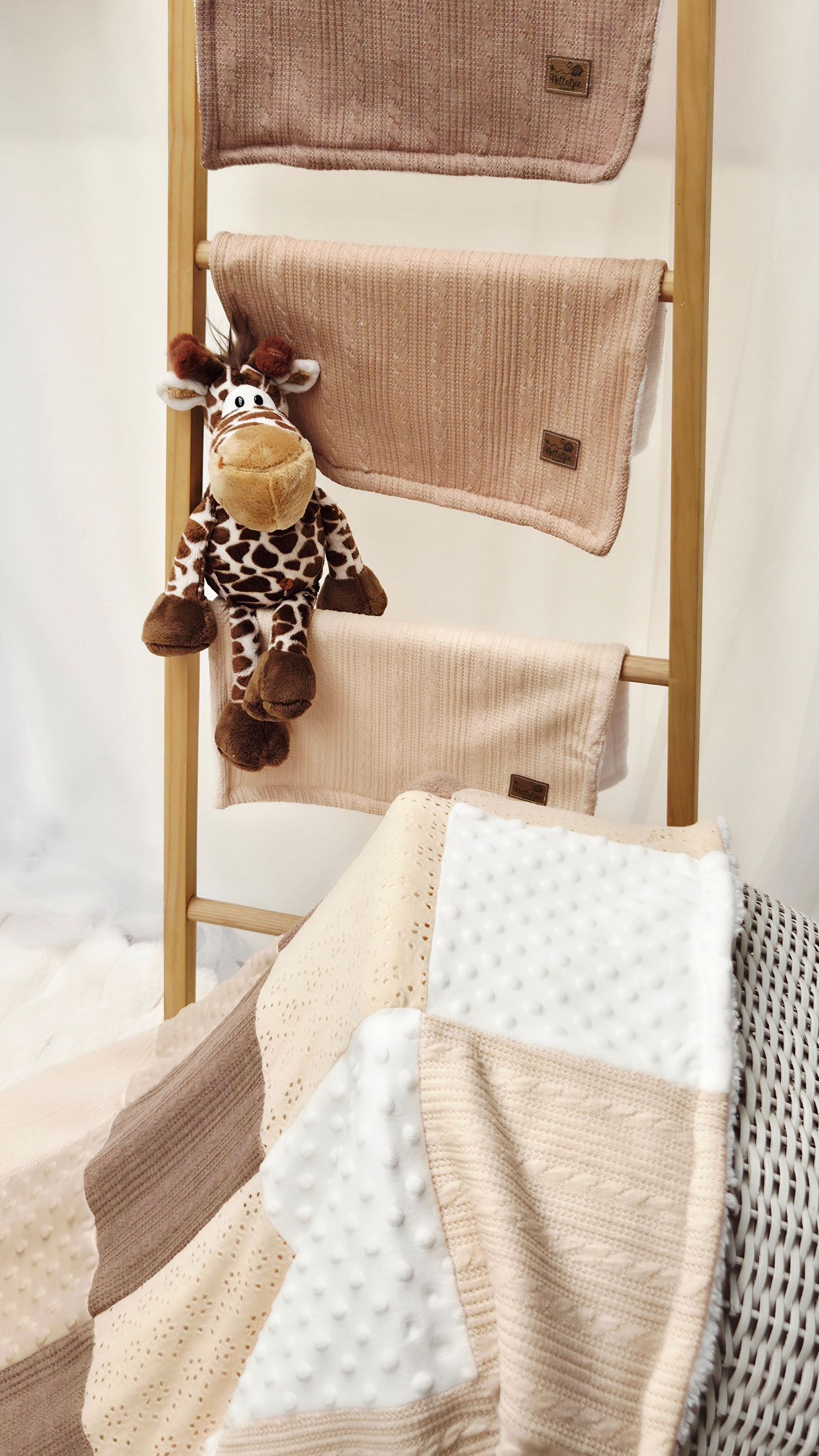 Decorative ladder with beige knit blankets and a plush giraffe toy, perfect for a cozy nursery display.