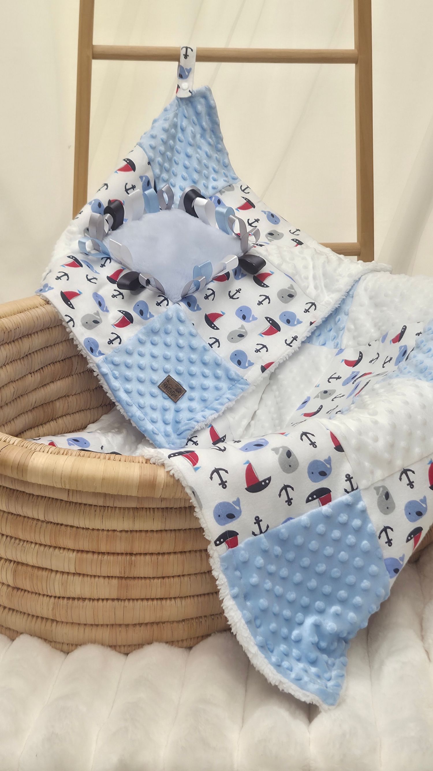 Blue minky baby blanket with nautical sailboat and anchor print, draped over a wicker basket.