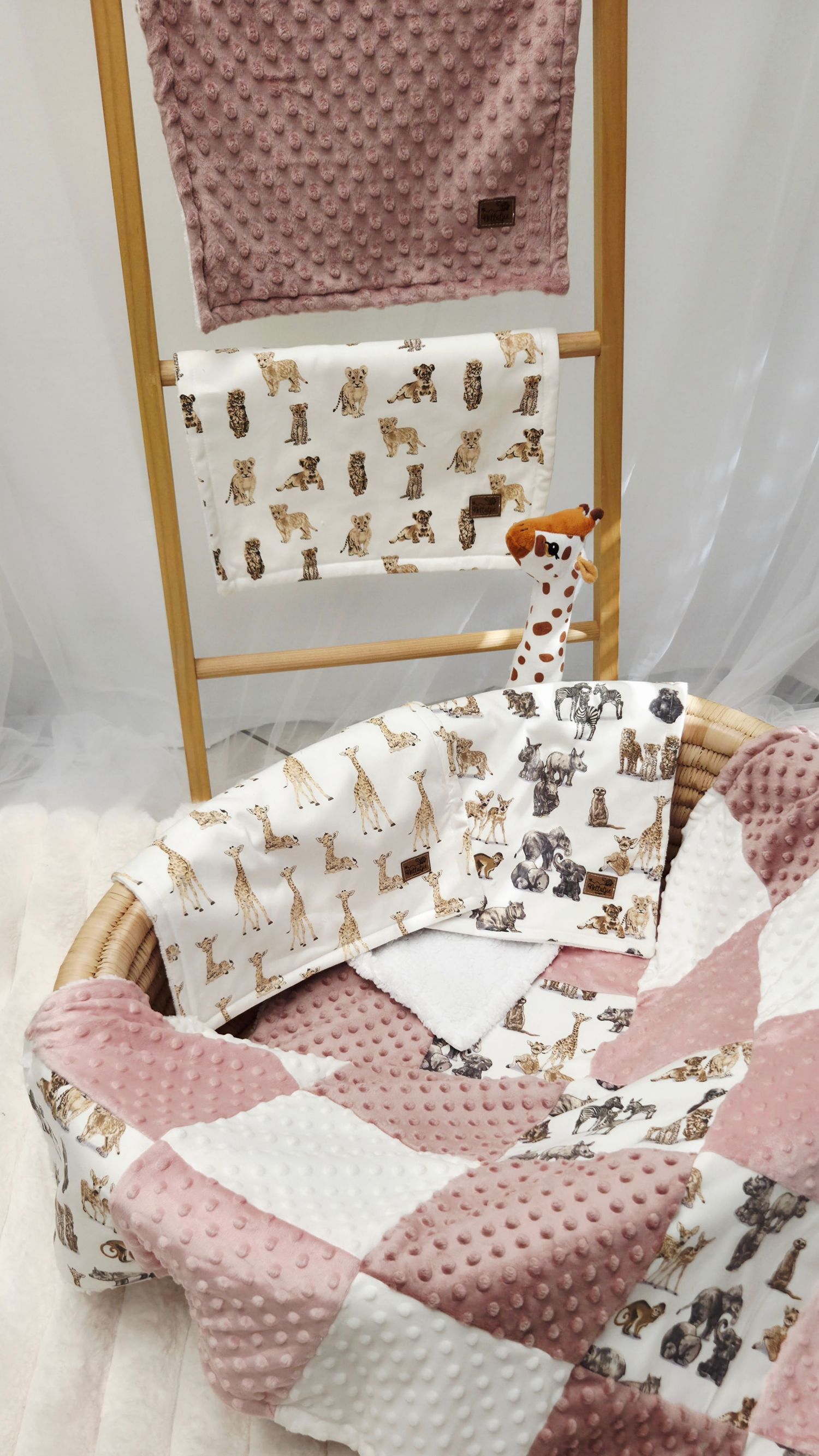 Pink minky patchwork baby quilt set with safari animal print blankets and giraffe toy in wicker basket.