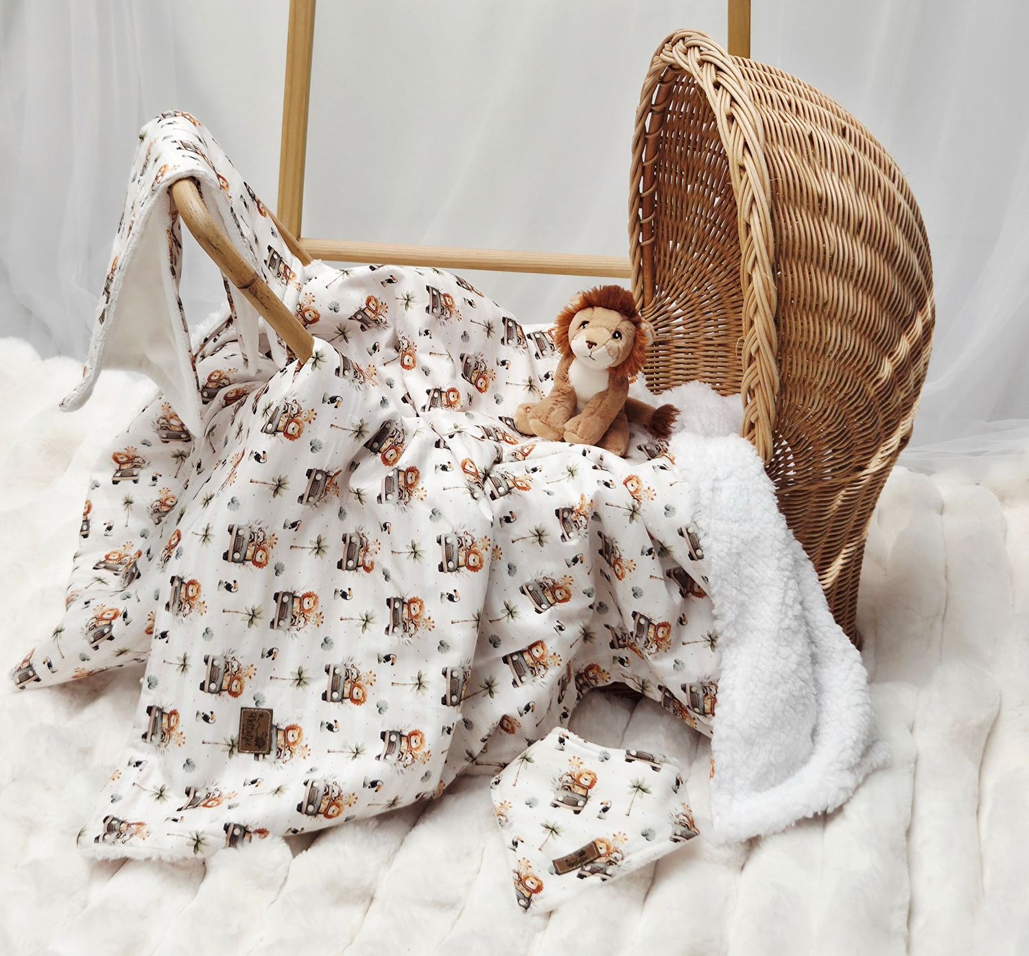 Baby blanket with teddy bear print draped over a wicker bassinet with a plush lion toy on a white fur rug.