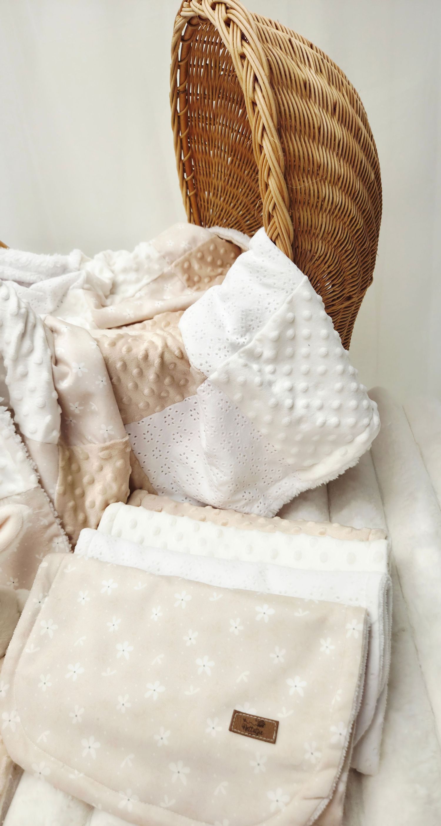 Soft pink and white baby blankets with minky dot texture neatly arranged in a wicker bassinet.