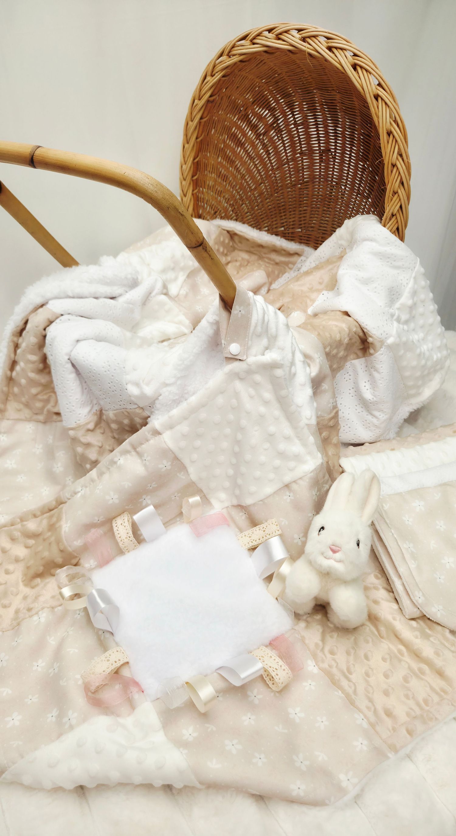 Soft baby gift set with white minky blanket, bunny toy, and taggy blanket beside a wicker bassinet.