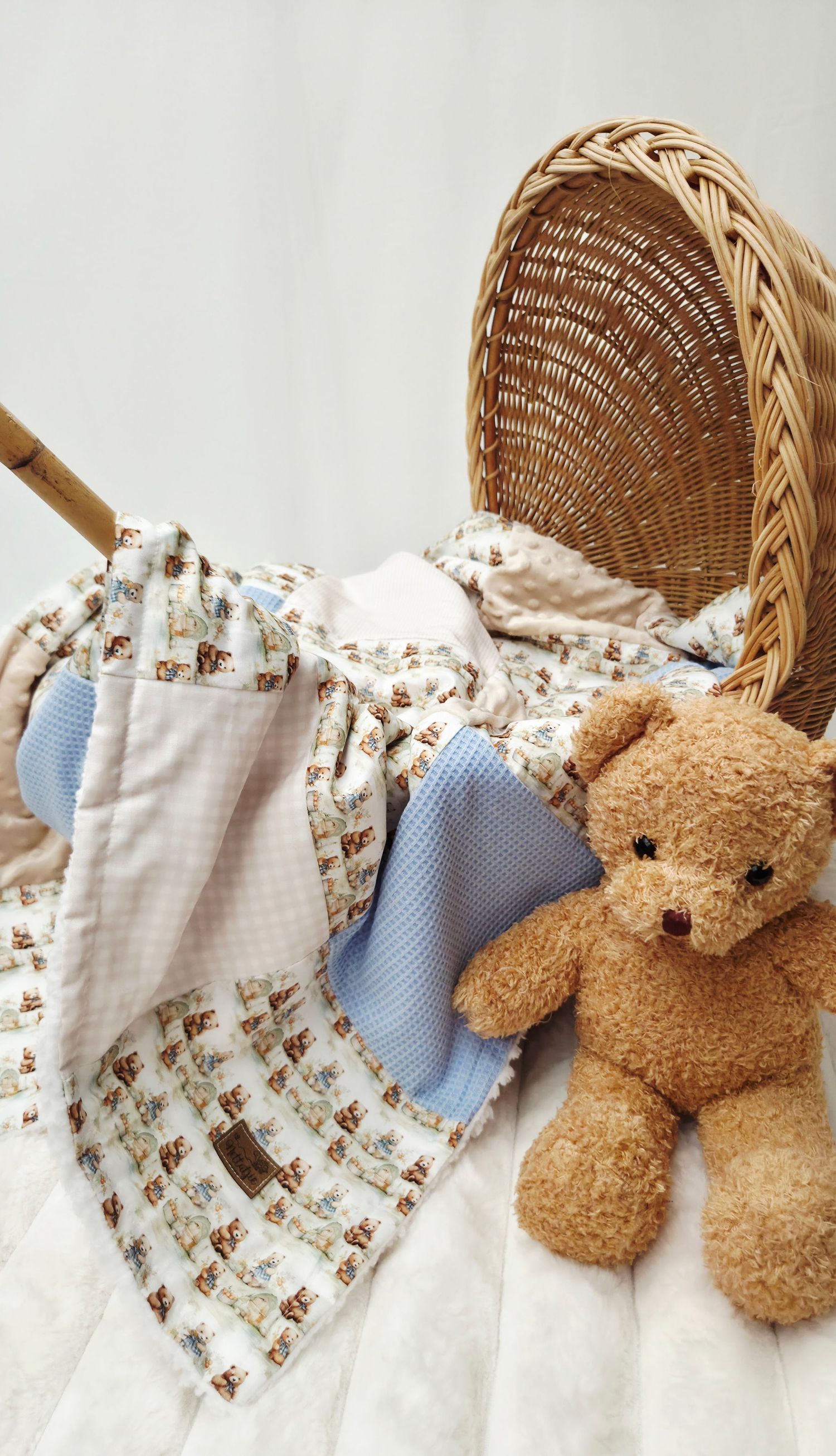 Cozy baby nursery scene with a brown teddy bear, patterned quilt blanket, and wicker basket on white background.