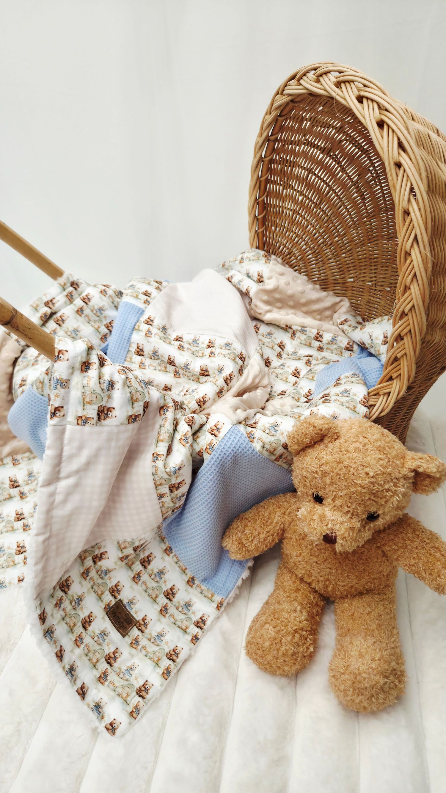Soft teddy bear with baby blankets featuring bear print beside a wicker bassinet on white background.