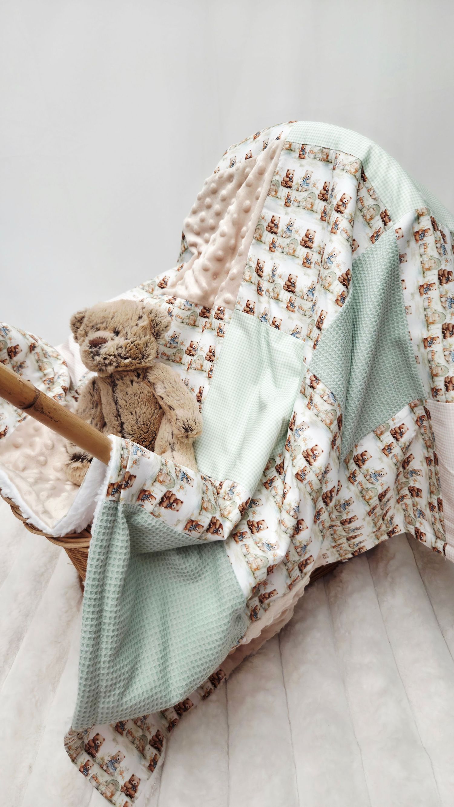 Soft mint green patchwork baby blanket with teddy bear print draped over wicker basket with plush bear toy.