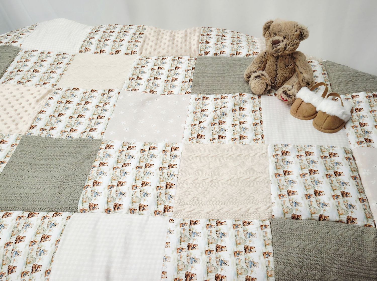 Handmade patchwork quilt in sage green and cream with floral prints, displayed flat with a classic teddy bear sitting on top.
