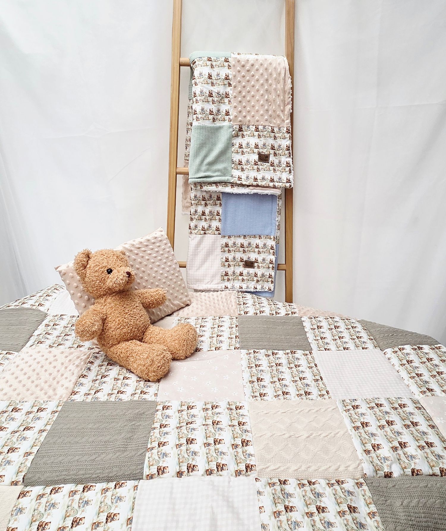 Handmade patchwork quilt with teddy bear print, paired with a stuffed bear toy and wooden ladder displaying matching blankets.