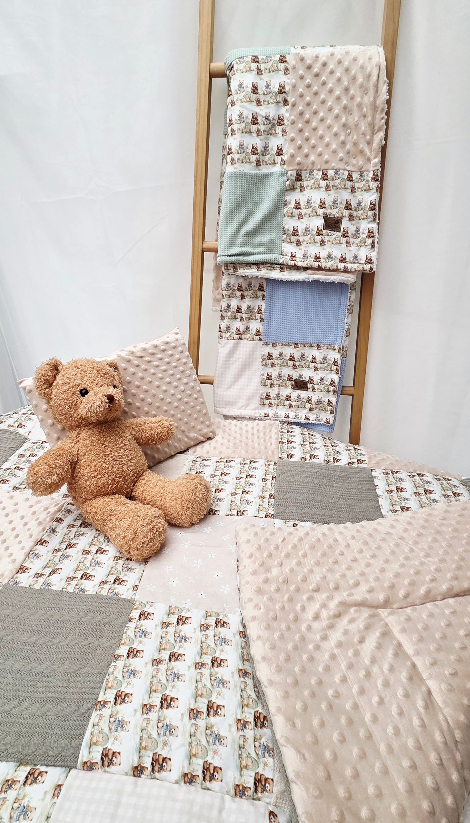 Handmade patchwork baby quilt set with teddy bear print, minky fabric, and matching blanket displayed on a wooden ladder.