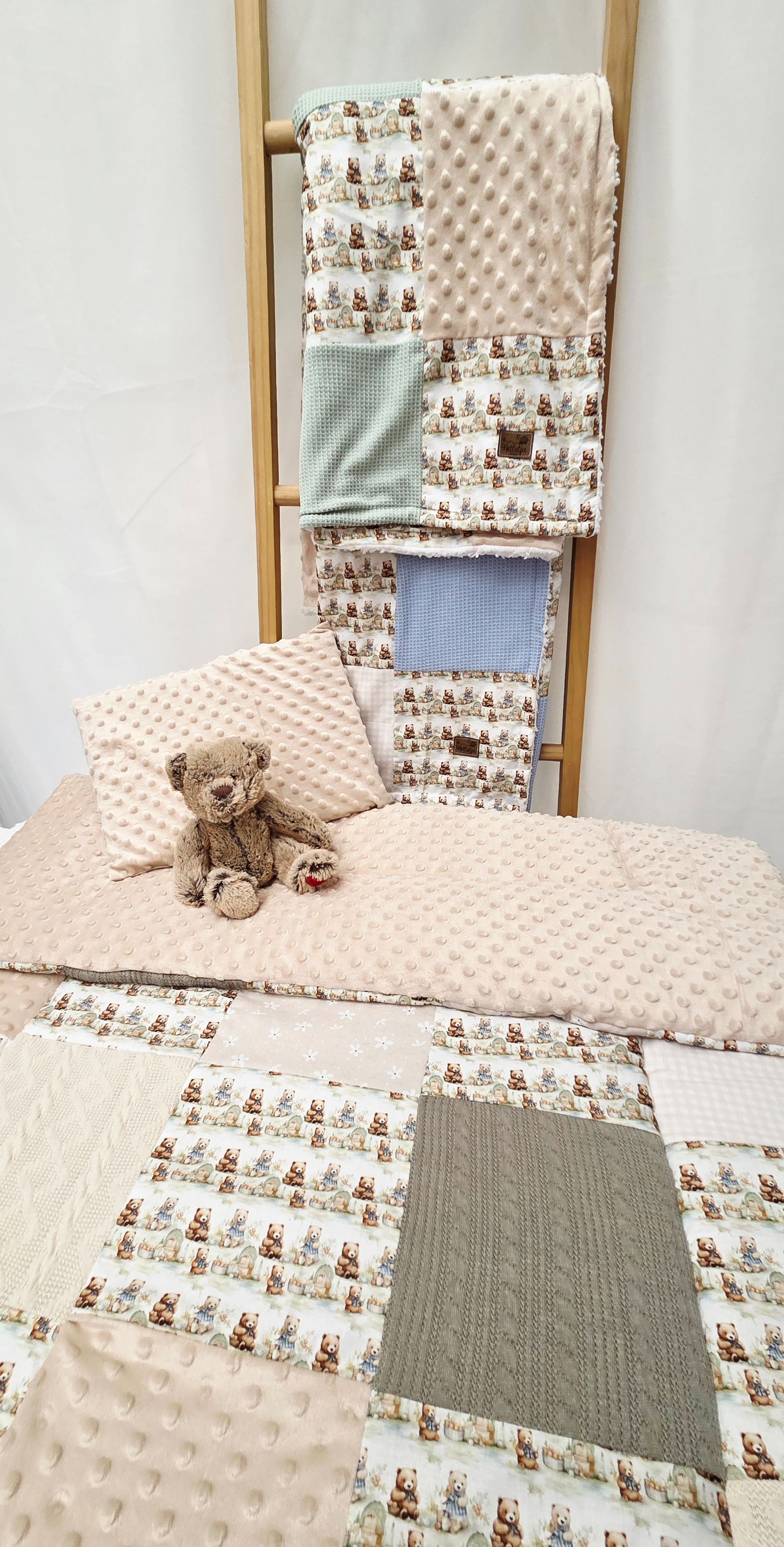 Handmade patchwork baby quilts in soft pastel tones with teddy bear print, displayed on a ladder with a plush bear toy.