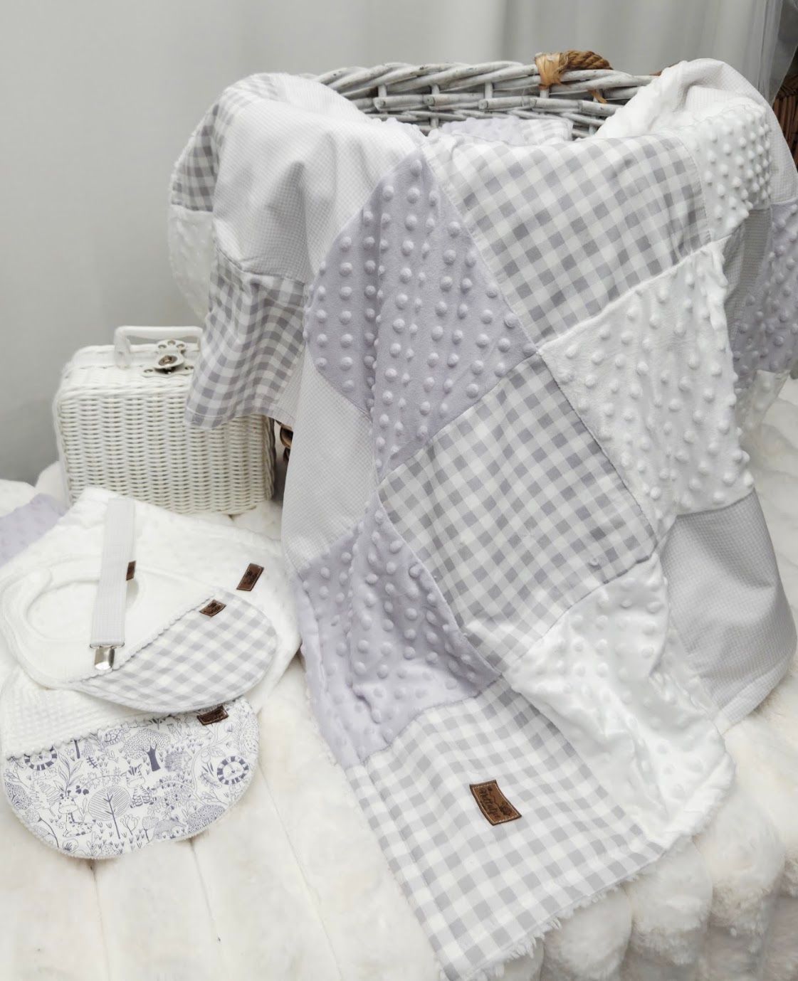 Gray and white gingham patchwork baby blanket with textured minky dots displayed with matching bib and wicker basket.
