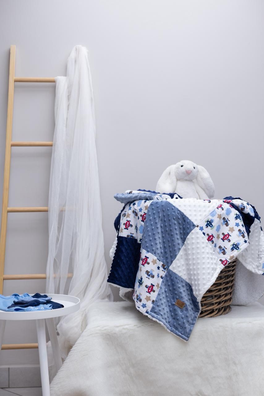 A navy and white quilted baby blanket with star pattern displayed on a bed with a decorative ladder in the background.