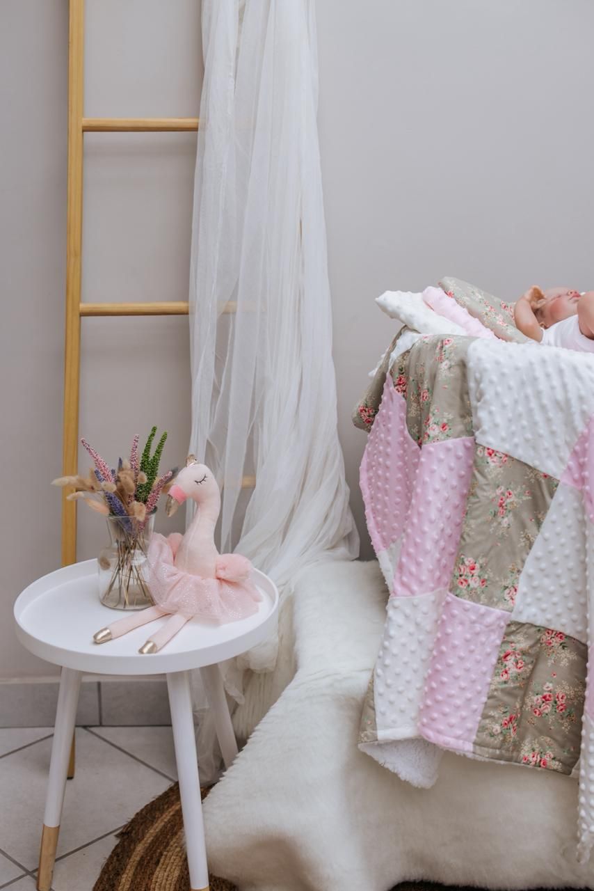 Pink minky blanket and floral fabric draped over white chair with tulle curtain in soft nursery decor setting.