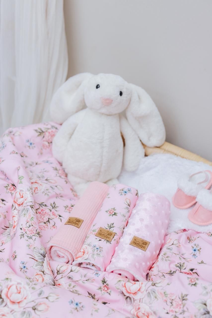Soft pink floral bedding with white plush bunny toys arranged on a bed.