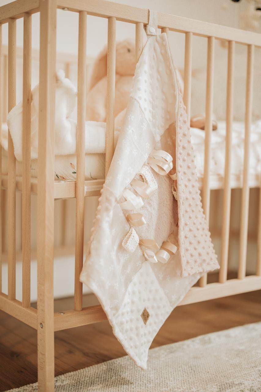 White lace and knit baby blankets hanging from a wooden crib railing in a nursery with hardwood floors.