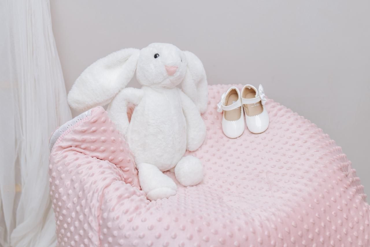 White plush bunny and tiny shoes displayed on pink textured bedding.