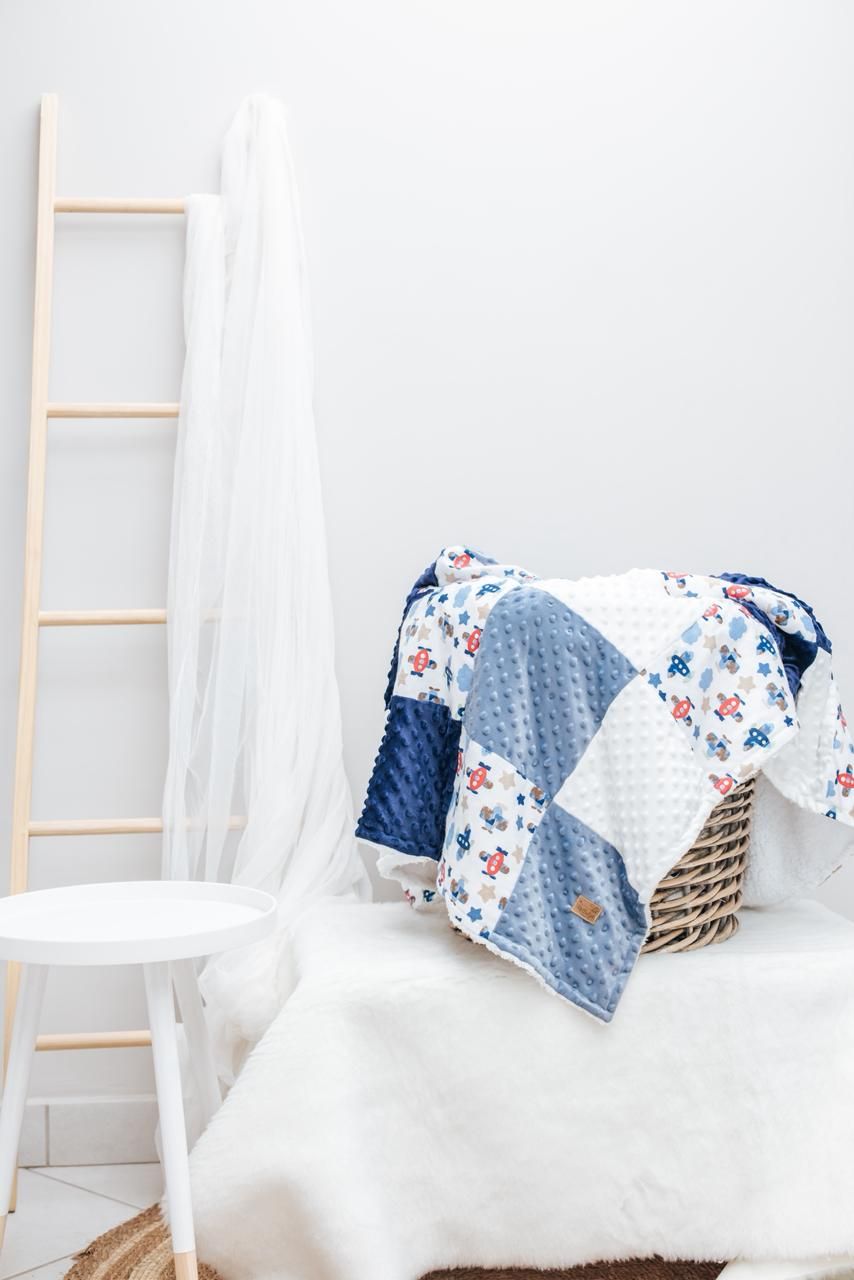 Cozy floral and blue quilted blanket draped over white furniture with a decorative wooden ladder in the background.