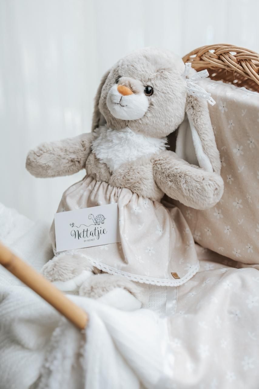 Soft white plush bunny toy with ribbon collar displayed on a gentle neutral background.